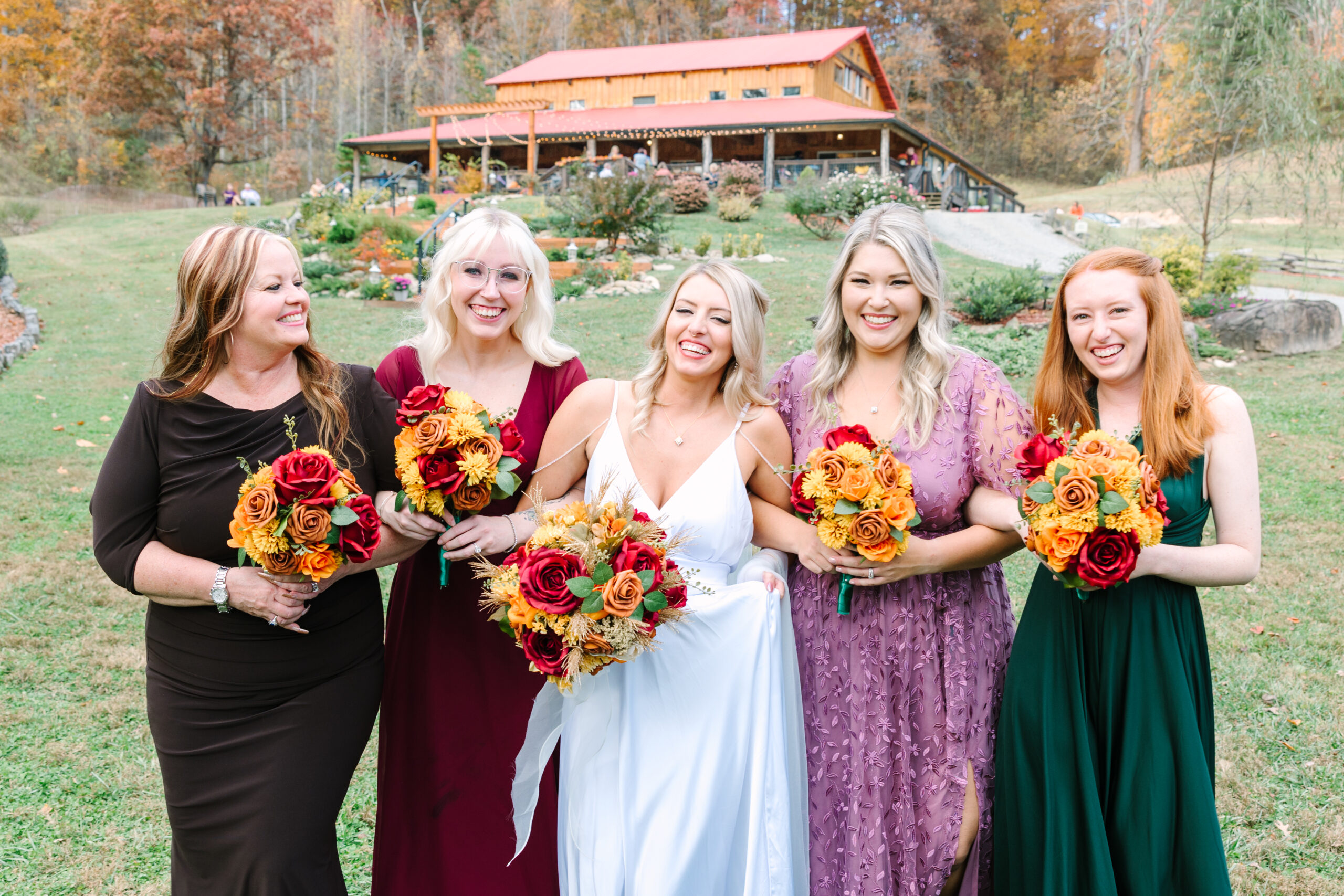 bride with fall color bridesmaid dresses in front of venue in mountains