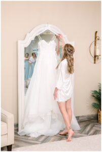 Bride admiring her wedding dress hanging on a mirror.