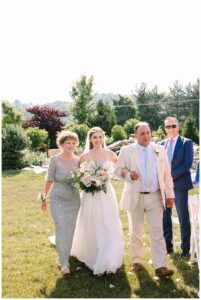 Bride walking down the aisle with her parents, holding a bouquet.