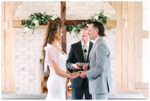 Bride and groom exchanging vows in front of a wooden cross decorated with flowers at Overlook Barn in Banner Elk, NC.