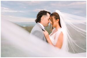 Bride and groom with their foreheads touching, surrounded by flowing veil, with a scenic mountain backdrop at Overlook Barn in Banner Elk, NC.