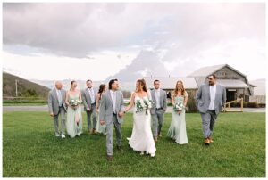 Bridal party walking together outside with the bride and groom holding hands, with rustic barn and mountain views at Overlook Barn in Banner Elk, NC.