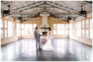 Bride and groom holding hands in a spacious indoor venue with large windows and string lights at Overlook Barn in Banner Elk, NC.