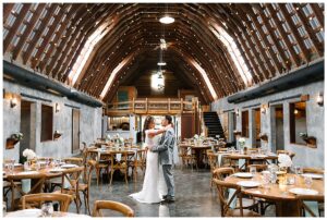 Bride and groom sharing a dance in the dining area of Overlook Barn, with tables set up and string lights hanging from the wooden beams in Banner Elk, NC.