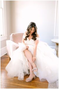 Bride sitting and smiling while adjusting her shoes at Vanlandingham Estate, Charlotte, NC.