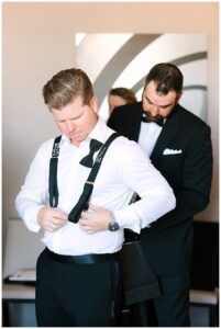 Groom adjusts his suspenders with the help of a groomsman at Vanlandingham Estate, Charlotte, NC.