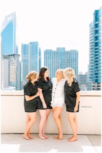 Bride and bridesmaids in matching pajamas on a rooftop with a cityscape background.