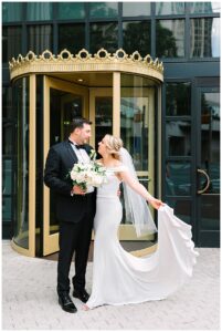 Bride and groom posing in front of a golden revolving door.