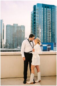 Bride and groom sharing a kiss on a rooftop with a cityscape background.