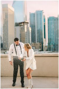 Bride and groom popping a champagne bottle on a rooftop.