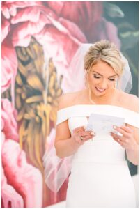 Bride reading a heartfelt letter in front of a floral mural.